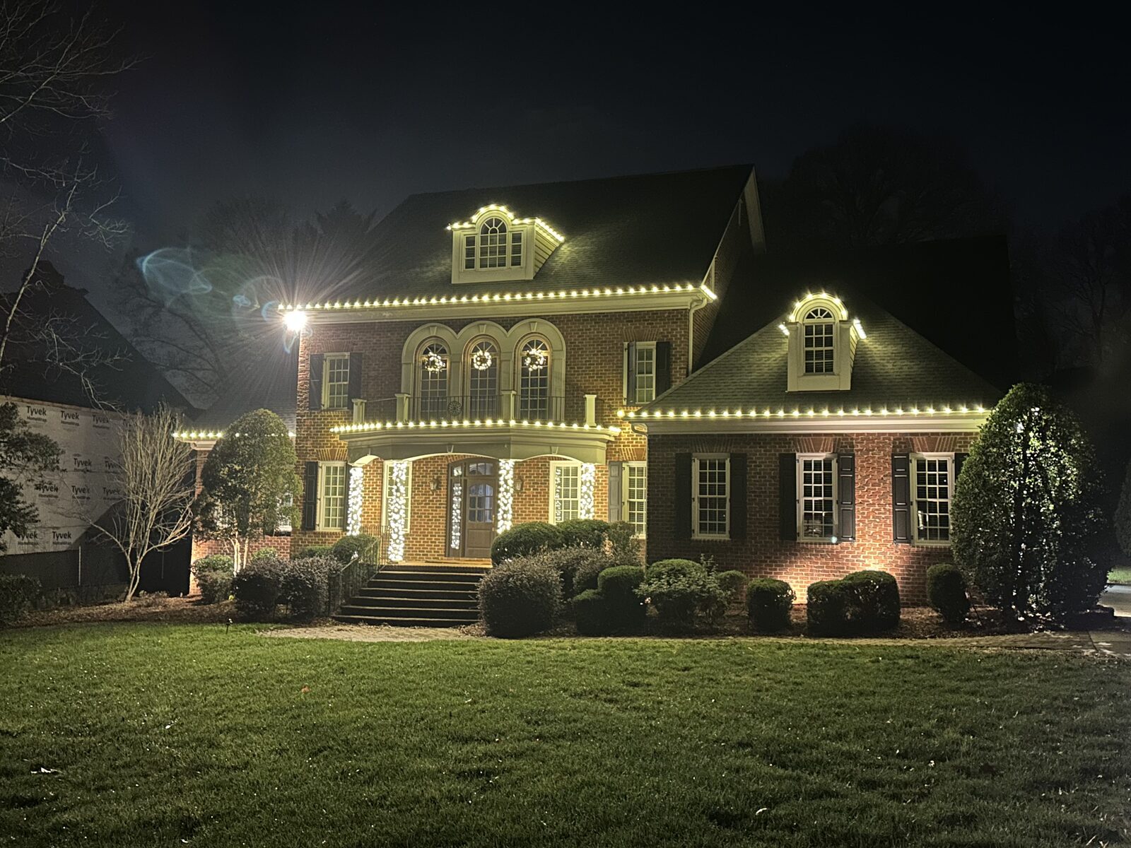 Brick two-story home in Charlotte outlined in warm white Christmas lights with lit entry columns and wreaths