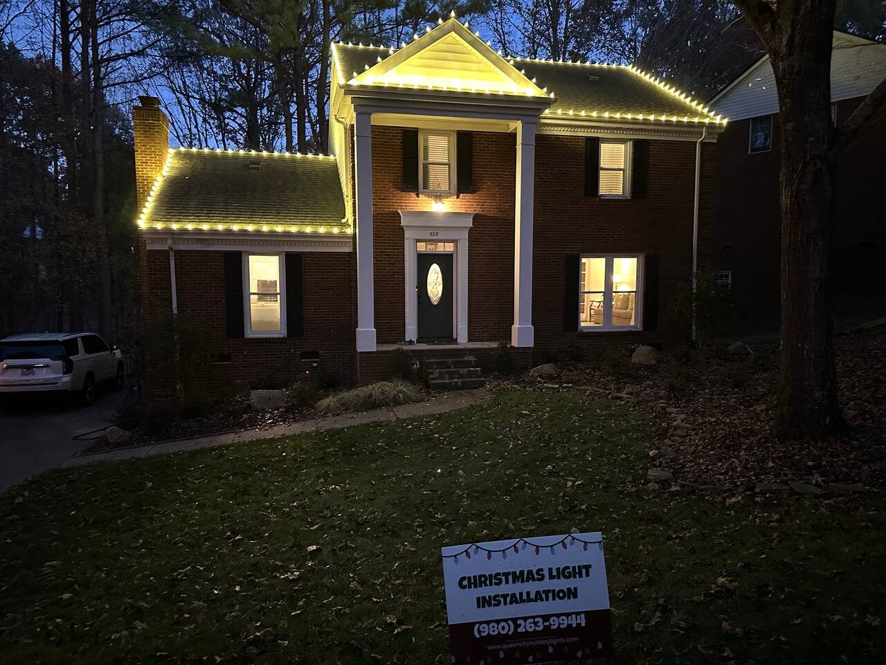Brick colonial home outlined in warm white roofline lights at dusk